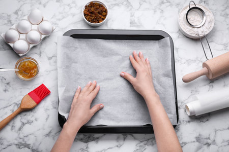 Woman putting parchment paper in baking pan at white marble table, top viewの写真素材