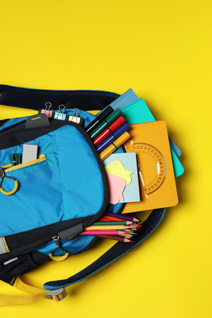 Backpack with school stationery on yellow background, top view. Space for textの写真素材