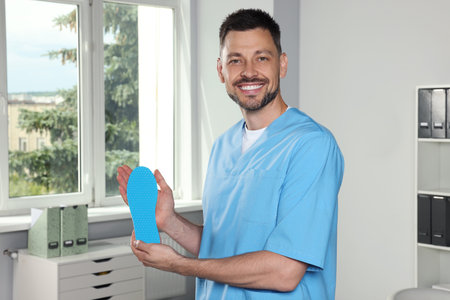 Handsome male orthopedist showing insole in hospitalの写真素材