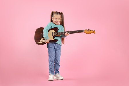 Happy girl with electric guitar on pink background. Space for textの写真素材