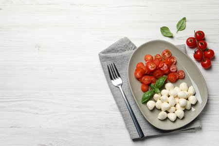 Delicious mozzarella balls, tomatoes and fork on white wooden table, flat lay. Space for textの写真素材