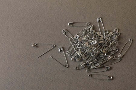 Pile of safety pins on gray textured background, flat lay