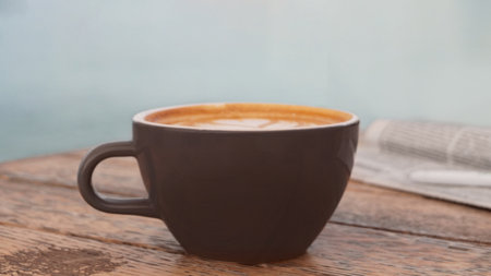 Cup of delicious coffee and newspaper on wooden table, closeup
