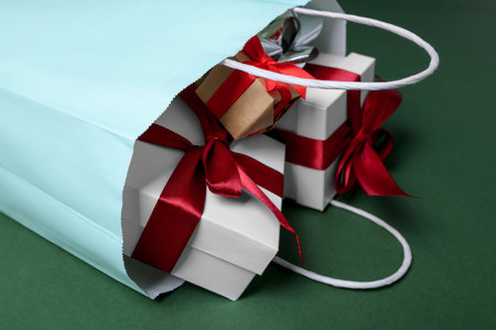 Turquoise paper shopping bag full of gift boxes on green background, closeupの写真素材