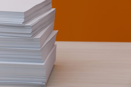 Stack of paper sheets on white wooden table near orange wall. Space for textの写真素材