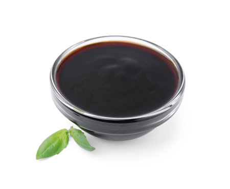 Glass bowl with balsamic glaze and basil leaves on white backgroundの写真素材