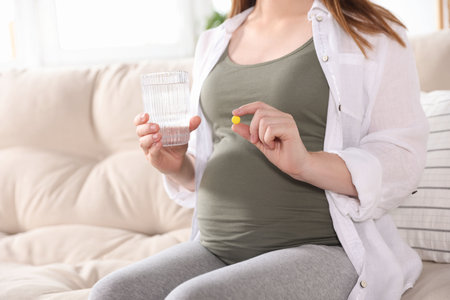 Pregnant woman holding pill and glass with water at home, closeupの写真素材