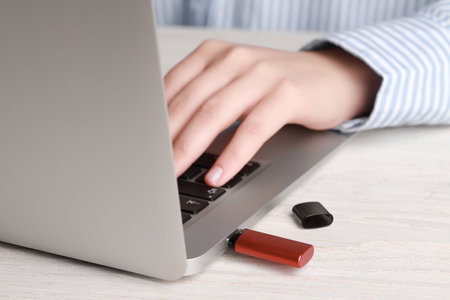 Woman using laptop with attached usb flash drive at wooden table, closeup