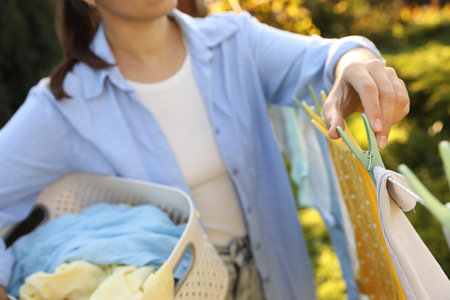 Woman hanging baby clothes with clothespins on washing line for drying in backyard, closeup