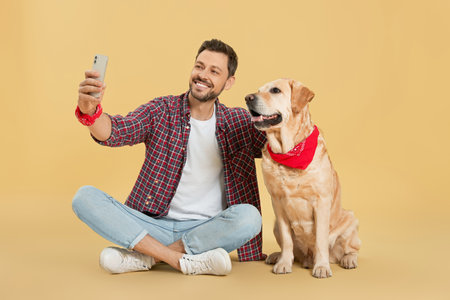 Man taking selfie with his cute Labrador Retriever on beige background