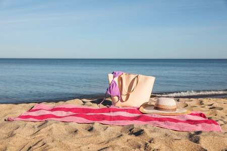 Beach towel with bag, straw hat and bikini on sand near sea, space for textの写真素材