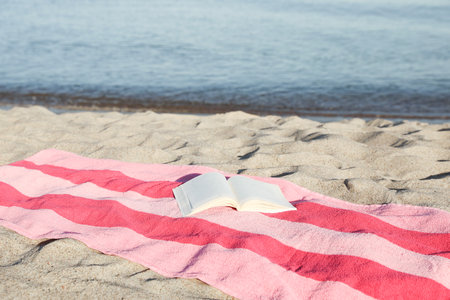 Beach towel and open book on sand near sea, space for textの写真素材