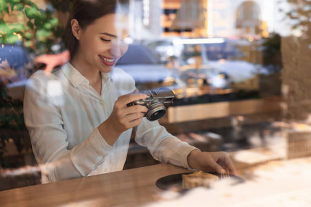 Young woman taking photo of plate with pie at cafe, view through window. creative hobbyの写真素材