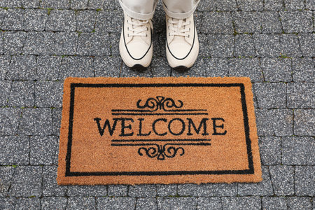 Woman near doormat with word Welcome on pavement outdoors, closeupの写真素材