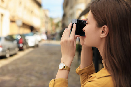 Young woman with camera taking photo on city street, space for text. interesting hobbyの写真素材