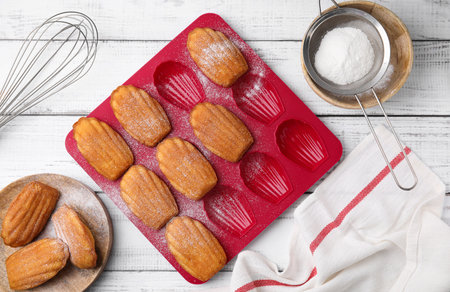 Delicious madeleine cookies and baking mold on white wooden table, flat layの写真素材