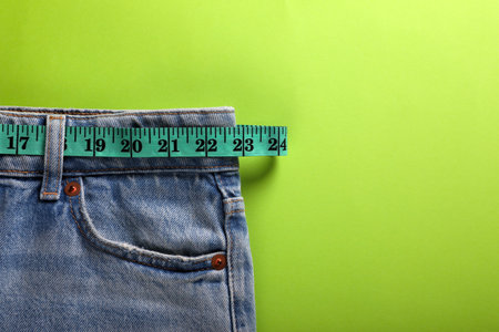 Jeans and measuring tape on light green background, top view with space for text. weight loss conceptの写真素材