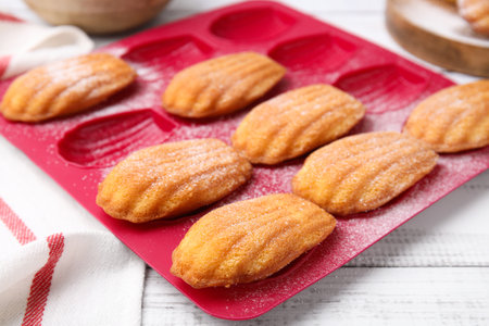 Delicious madeleine cookies in baking mold on white wooden table, closeupの写真素材