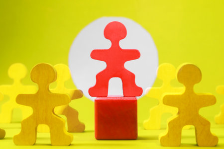 Wooden figures with red one on yellow background, closeup. Recruiter searching employeeの写真素材