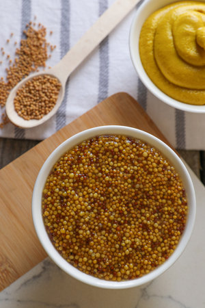 Bowls and spoon of whole grain mustard on wooden table, flat lay