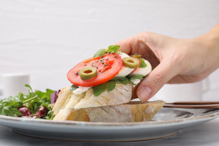 Woman taking tasty bruschetta with tomatoes, mozzarella and olives from plate, closeupの写真素材