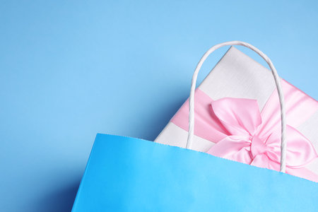 Bright paper shopping bag with gift box on light blue background, top view. Space for textの写真素材