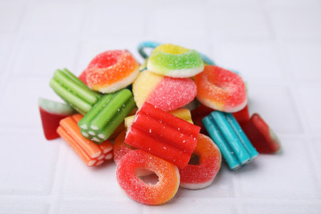 Pile of tasty colorful jelly candies on white tiled table, closeup