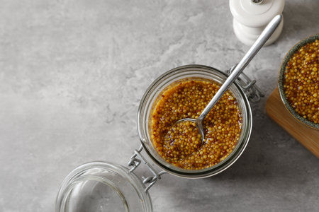 Bowl and jar of delicious whole grain mustard on gray table, flat lay. Space for text