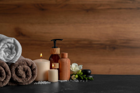 Beautiful spa composition with different care products and burning candles on black table. Space for...