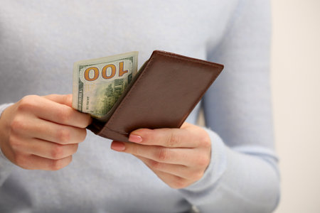 Woman holding brown leather wallet with 100 dollar bill on white background, closeup. money exchange