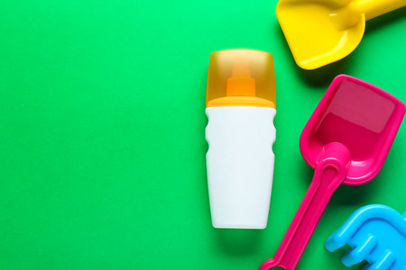 Bottle of suntan cream and children's beach toys on green background, flat lay. Space for textの写真素材