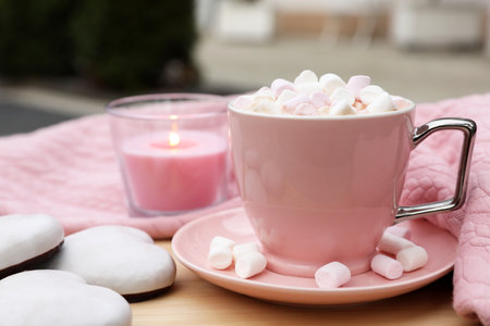Cup of tasty cocoa with marshmallows, pink sweater, cookies and burning candle on wooden table outdoorsの写真素材