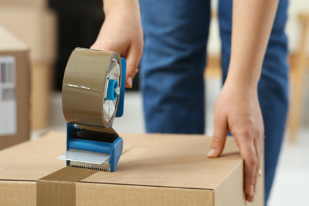Woman applying adhesive tape on box with dispenser indoors, closeupの写真素材