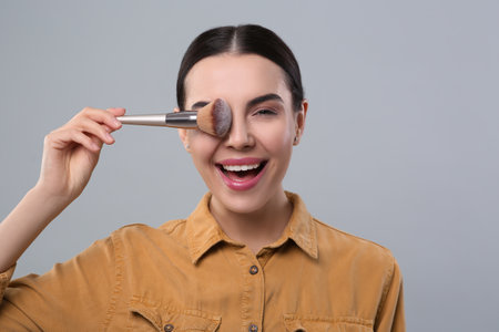 Happy woman with makeup brush on light gray backgroundの写真素材