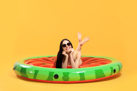 Happy young woman with beautiful suntan and sunglasses on inflatable mattress against orange...