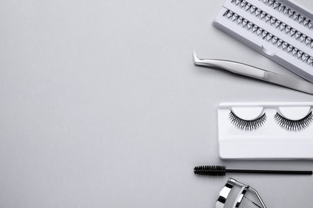 Flat lay composition with fake eyelashes, brush and tools on light gray background. Space for text