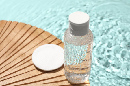 Wet bottle of micellar water and cotton pad on wooden board, closeupの写真素材
