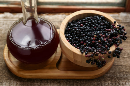 Elderberry wine and bowl with Sambucus berries on wooden table