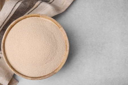 Granulated yeast in wooden bowl on light gray table, top view. Space for textの写真素材