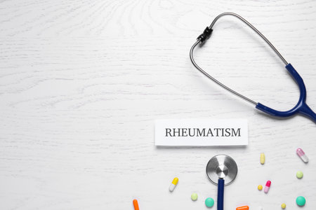 Card with word Rheumatism, stethoscope and pills on white wooden table, flat lay. Space for textの写真素材