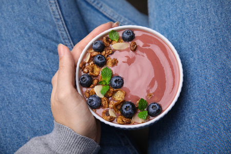 Woman holding bowl of delicious fruit smoothie with fresh blueberries and granola, top viewの写真素材