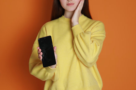 Woman showing damaged smartphone on orange background, closeup. device repair