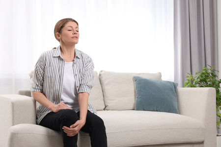 Woman suffering from knee pain on sofa indoors. arthritis symptomsの写真素材