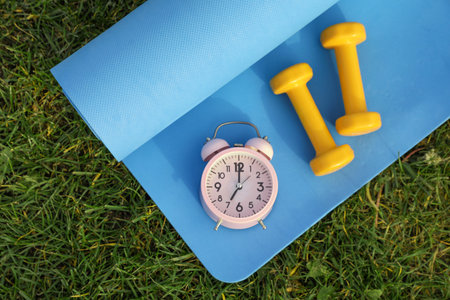 Alarm clock, dumbbells and fitness mat on green grass, flat lay. morning exerciseの写真素材