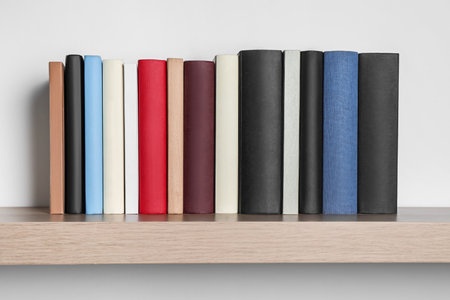 Many hardcover books on wooden shelf near white wallの写真素材