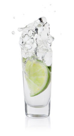 Vodka splashing out of shot glass with lime on white backgroundの写真素材