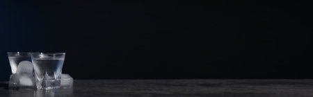 Vodka in shot glasses with ice on black table against dark background, space for text. banner designの写真素材
