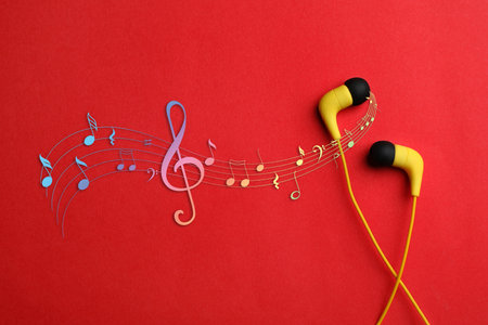 Staff with music notes and treble clef flowing from yellow earphones on red background, top viewの写真素材