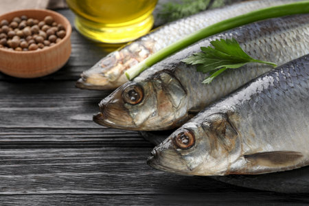 Delicious salted herrings and ingredients on black wooden table, closeup
