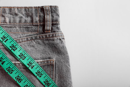Jeans with measuring tape on light gray background, top view and space for text. weight loss conceptの写真素材
